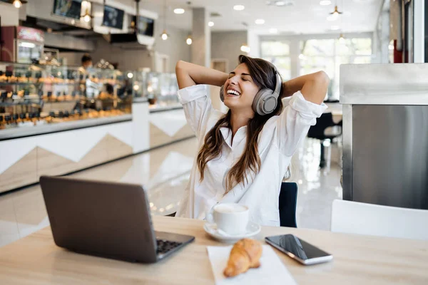 Güzel ve mutlu genç bir kadın fırında ya da fast food 'da oturup lezzetli börekler yiyor. Ayrıca laptopunu kullanıyor ve kulaklıkla müzik dinliyor.. 