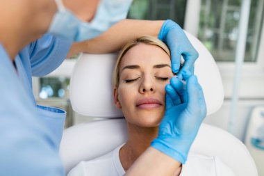 Çekici kadın güzellik kliniğinde gençleştirici yüz enjeksiyonu yaptırıyor. Güzellik uzmanı kadın kırışıklıklarını botulinyumla dolduruyor..