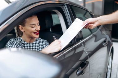 Yeni arabasında oturan tatmin olmuş ve gülümseyen bayan alıcı. İkinci el araba satıcısıyla alıcı sözleşmesi imzalarken mutlu oluyor..
