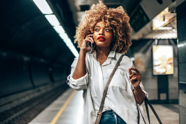 美丽时髦的黑人妇女站在地铁站 她很高兴 用她的智能手机和别人说话 公共交通和城市生活概念 — 图库照片
