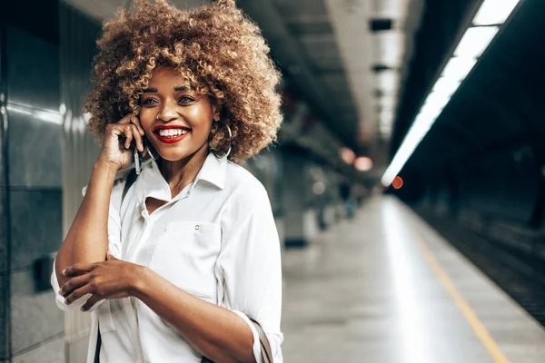 美丽时髦的黑人妇女站在地铁站 她很高兴 用她的智能手机和别人说话 公共交通和城市生活概念 — 图库照片