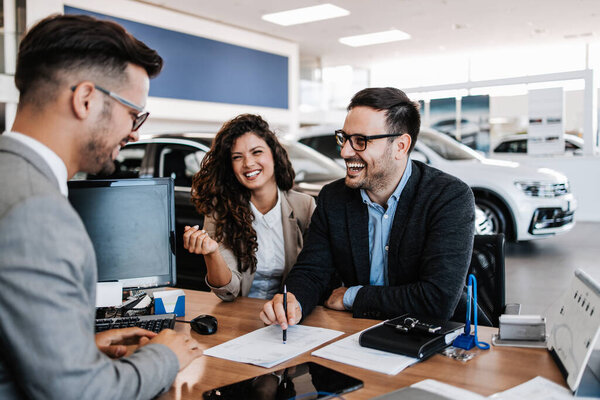 Middle age couple choosing and buying car at car showroom. Car salesman helps them to make right decision. Man signs buyers contract.