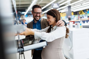 Beautiful and happy middle age couple buying consumer tech products in modern home appliances store. They are choosing electrical cooker and oven. People and consumerism concept.