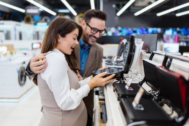 Beautiful and happy middle age couple buying consumer tech products in modern home tech store. They are choosing small kitchen appliances. People and consumerism concept.