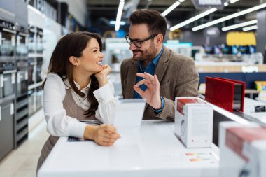 Beautiful and happy middle age couple buying consumer tech products in modern home appliances store. They are choosing washing or cloth dryer machine. People and consumerism concept.