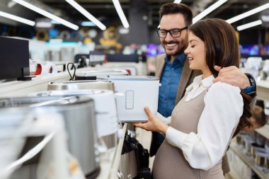 Beautiful and happy middle age couple buying consumer tech products in modern home tech store. They are choosing small kitchen appliances. People and consumerism concept.