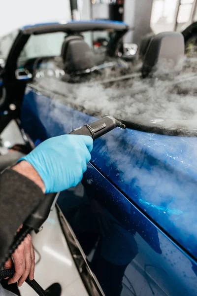 Professional vehicle detailing service in a modern car workshop. Car workshop specialist putting vinyl foil or film on car. Worker using steam pistol for better wrapping and tightening foil edges.