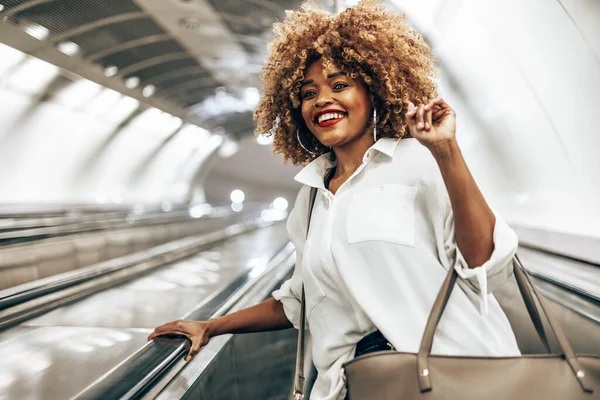 美丽的黑人妇女站在自动扶梯上 前往灯光明亮的现代化地铁站 公共交通和城市生活概念 低角度射击 — 图库照片