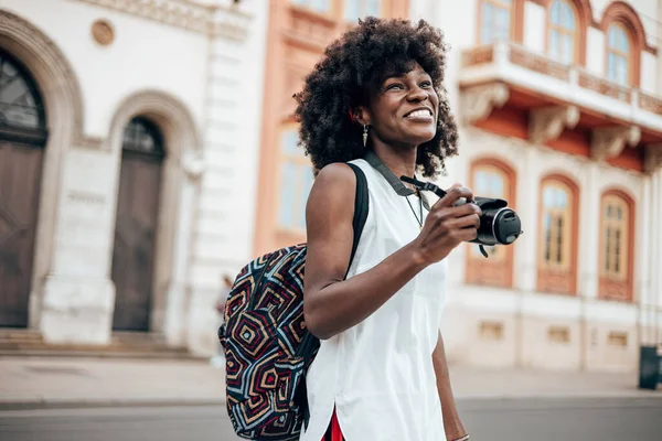 Genç siyah bayan turist güzel bir Avrupa şehrinin sokaklarında yürümekten zevk alıyor. O mutlu ve fotoğraf makinesini fantastik mimari fotoğraflar çekmek için kullanıyor. Parlak güneşli bir gün.