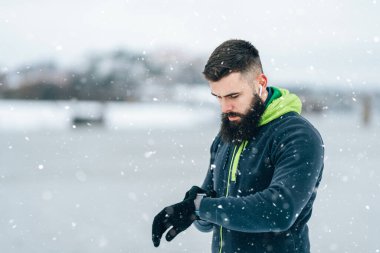 Çok soğuk ve karlı bir günde sakallı, koşan ve dışarıda egzersiz yapan yakışıklı orta yaşlı bir adam. Spor ve spor motivasyon teması. Aktivite verilerini takip etmek için akıllı saat kullanıyor..