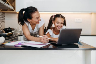 Genç bir anne, virüs salgını sırasında ya da karantinada kızına e-öğrenim oturumunda yardım ediyor. Hastalık önleme ve yeni normal kavram.