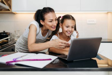 Genç bir anne, virüs salgını sırasında ya da karantinada kızına e-öğrenim oturumunda yardım ediyor. Hastalık önleme ve yeni normal kavram.