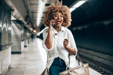 Güzel, modaya uygun siyah kadın metro istasyonunda duruyor. O mutlu ve akıllı telefonundan biriyle konuşuyor. Toplu taşıma ve kentsel yaşam konsepti.