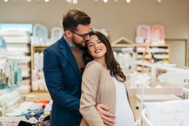 Attractive middle age couple enjoying in buying clothes and appliances for their new baby. Heterosexual couple in baby shop or store. Expecting baby concept.