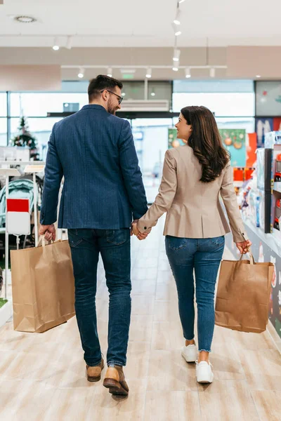 満足し幸せなカップルは赤ちゃんの店でショッピングバッグ 親と子供は概念を期待する バックビュー — ストック写真