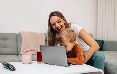 Küçük oğluyla oynayan mutlu orta yaşlı kadın. Onlar oynamak, öğrenmek ve çevrimiçi sörf yapmak için akıllı telefon ve dizüstü bilgisayar kullanıyorlar..