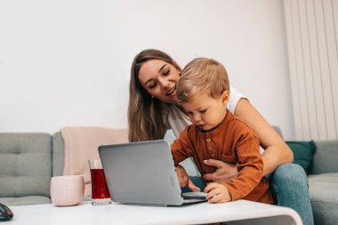 Küçük oğluyla oynayan mutlu orta yaşlı kadın. Onlar oynamak, öğrenmek ve çevrimiçi sörf yapmak için akıllı telefon ve dizüstü bilgisayar kullanıyorlar..