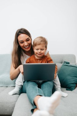 Küçük oğluyla oynayan mutlu orta yaşlı kadın. Onlar oynamak, öğrenmek ve çevrimiçi sörf yapmak için akıllı telefon ve dizüstü bilgisayar kullanıyorlar..