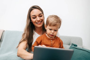 Küçük oğluyla oynayan mutlu orta yaşlı kadın. Onlar oynamak, öğrenmek ve çevrimiçi sörf yapmak için akıllı telefon ve dizüstü bilgisayar kullanıyorlar..