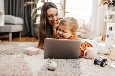 Küçük oğluyla oynayan mutlu orta yaşlı kadın. Onlar oynamak, öğrenmek ve çevrimiçi sörf yapmak için akıllı telefon ve dizüstü bilgisayar kullanıyorlar..