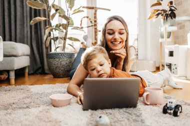 Küçük oğluyla oynayan mutlu orta yaşlı kadın. Onlar oynamak, öğrenmek ve çevrimiçi sörf yapmak için akıllı telefon ve dizüstü bilgisayar kullanıyorlar..