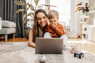 Küçük oğluyla oynayan mutlu orta yaşlı kadın. Onlar oynamak, öğrenmek ve çevrimiçi sörf yapmak için akıllı telefon ve dizüstü bilgisayar kullanıyorlar..