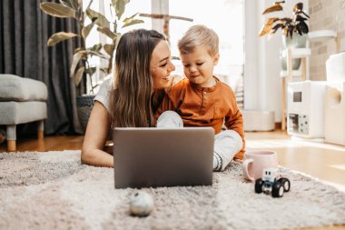 Küçük oğluyla oynayan mutlu orta yaşlı kadın. Onlar oynamak, öğrenmek ve çevrimiçi sörf yapmak için akıllı telefon ve dizüstü bilgisayar kullanıyorlar..