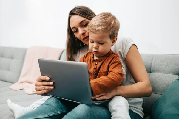 stock image Happy middle age woman playing with her little son at home. They are using smart phone and laptop computer for playing, learning and online surfing.