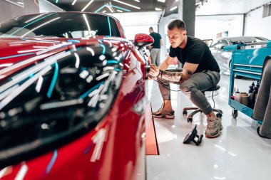 Modern bir araba atölyesinde profesyonel araç cilalama ve detay verme servisi. Parlak ışıklandırılmış çalışma alanı, büyük ışıklı. Yüksek kaliteli araba valelik kavramı.