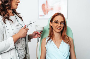 Otolaryngologist doing ear irrigation and earwax removal to a young adult woman with modern medical equipment. Healthcare and medicine concept. 