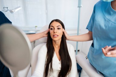Güzellik kliniğindeki güzel ve mutlu esmer kadın. Oturup iki kadın doktorla yüz estetiği hakkında konuşuyor..