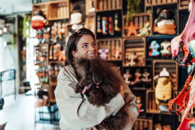Güzel genç bir kadın, sevimli kahverengi oyuncak kanişiyle modern evcil hayvan dükkanında eğleniyor.. 