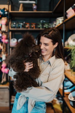Güzel genç bir kadın, sevimli kahverengi oyuncak kanişiyle modern evcil hayvan dükkanında eğleniyor.. 