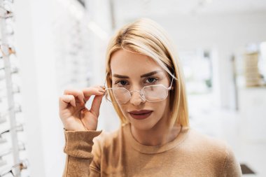 Modern optik mağazada gözlük çerçevesi seçen güzel ve şık bir kadın.. 