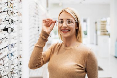 Modern optik mağazada gözlük çerçevesi seçen güzel ve şık bir kadın.. 