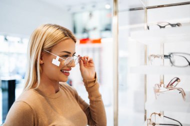 Modern optik mağazada gözlük çerçevesi seçen güzel ve şık bir kadın.. 
