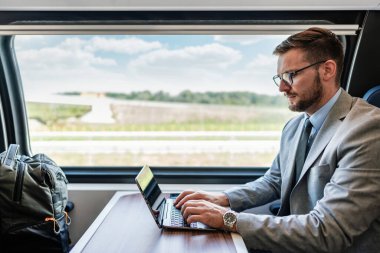 Hızlı trenle seyahat ederken dizüstü bilgisayarını kullanan orta yaşlı yakışıklı bir iş adamı. Modern ve hızlı seyahat kavramı.