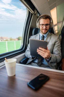 Yakışıklı iş adamı yüksek hızlı trenle seyahat ederken iyi vakit geçiriyor. Çevrimiçi iletişim, oyun ve eğlence için dizüstü bilgisayar ve kablosuz kulaklık kullanıyor.