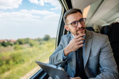 Hızlı trenle seyahat ederken dizüstü bilgisayarını kullanan orta yaşlı yakışıklı bir iş adamı. Modern ve hızlı seyahat kavramı.