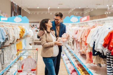 Attractive middle age couple enjoying in buying clothes and appliances for their new baby. Heterosexual couple in baby shop or store. Expecting baby concept.