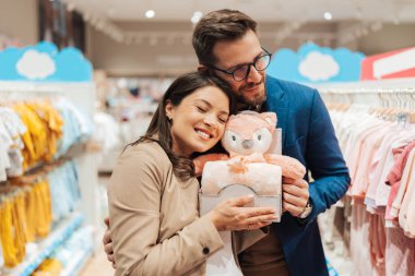 Attractive middle age couple enjoying in buying clothes and appliances for their new baby. Heterosexual couple in baby shop or store. Expecting baby concept.