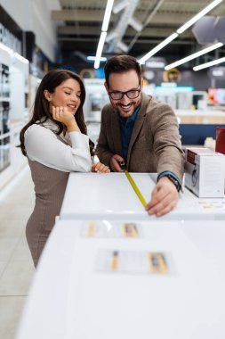 Beautiful and happy middle age couple buying consumer tech products in modern home appliances store. They are choosing washing or cloth dryer machine. People and consumerism concept.