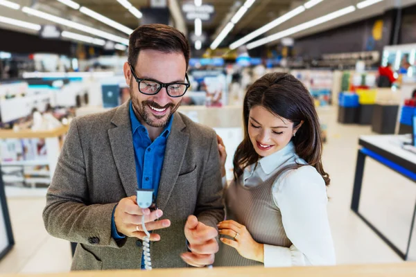 Beautiful and happy middle age couple buying consumer tech products in modern home appliances store. They are choosing beard and hair clipper and hairdryer. People and consumerism concept.
