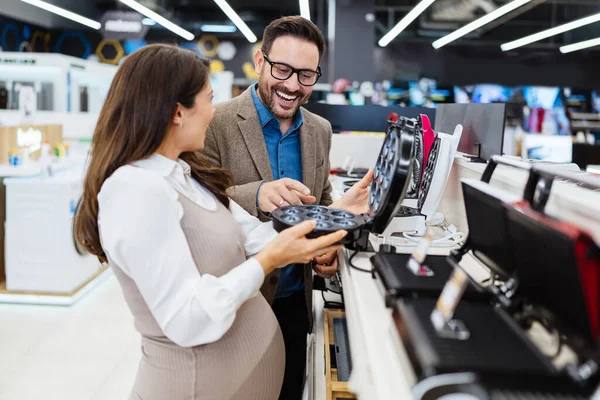 Beautiful and happy middle age couple buying consumer tech products in modern home tech store. They are choosing small kitchen appliances. People and consumerism concept.