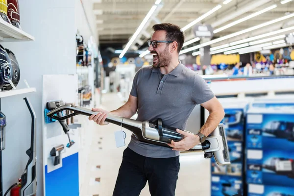 Yakışıklı orta yaşlı satıcı ev aletleri ve elektronik mağazasında çalışıyor. Mutludur ve elektrikli süpürge ile gitar çalar gibi oynar.