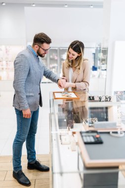 Zarif orta yaşlı işadamı yeni pahalı saatini seçip alıyor. Güzel, genç bir bayan satıcı iyi bir karar vermesine yardımcı olur. Moda tarzı ve zarafet konsepti.