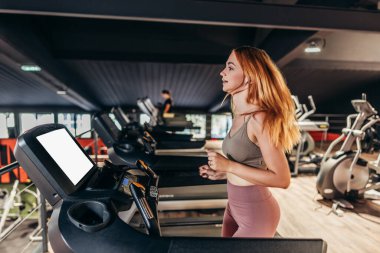 Güzel, genç, kızıl saçlı kadın geniş ve modern bir spor salonunda egzersiz yapıyor. İnsanlar ve eğlence konsepti.