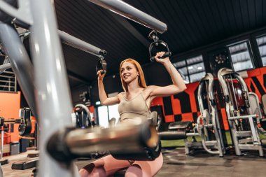 Güzel, genç, kızıl saçlı kadın geniş ve modern bir spor salonunda egzersiz yapıyor. İnsanlar ve eğlence konsepti.