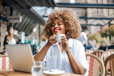 Güzel siyahi iş kadını restoranda ya da kafe barda oturuyor ve bilgisayarını online iletişim ya da kurumsal görüntülü sohbet için kullanıyor. Parlak güneşli bir gün.