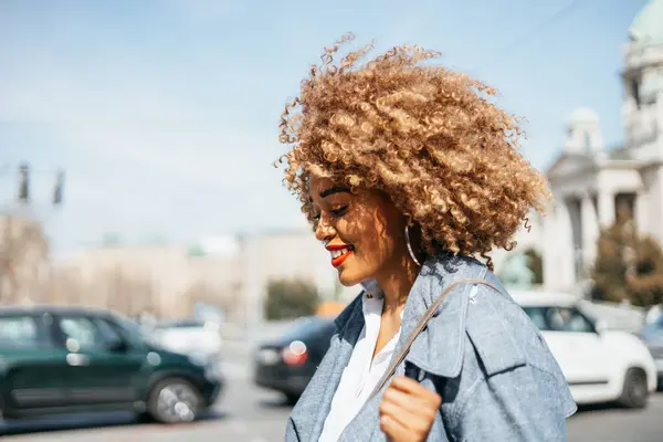 Beautiful and confident black woman walking down the street. She is happy and smiled. Bright sunny day. Side view.